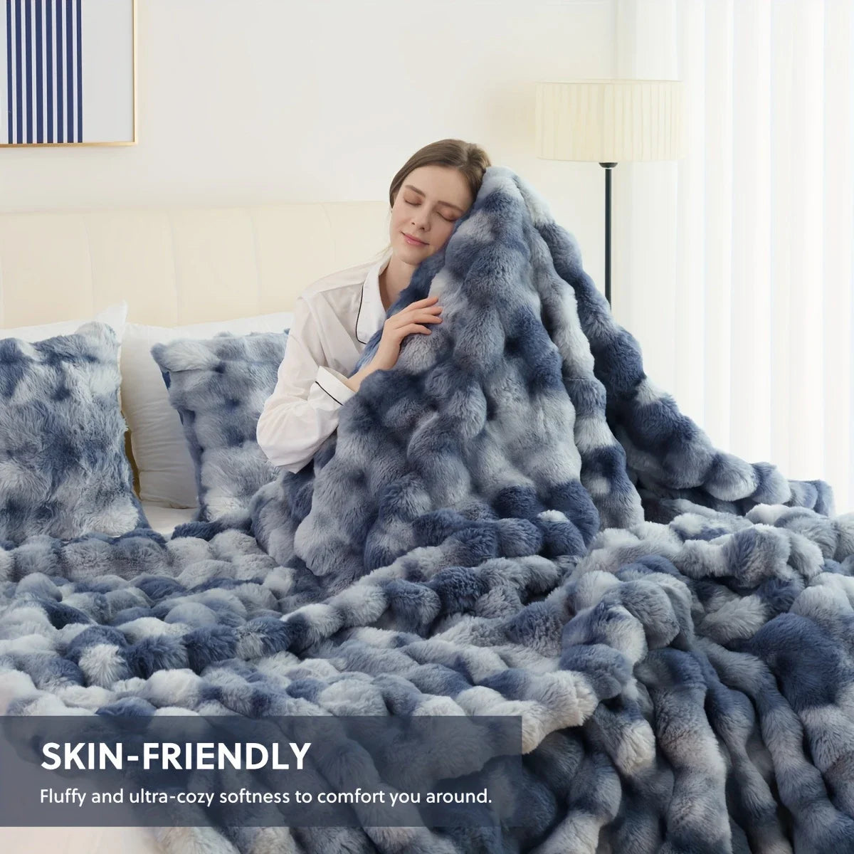 Person wrapped in a fluffy, blue blanket with text 'SKIN-FRIENDLY' on a bed.