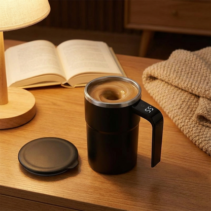 Black mug with handle on a wooden surface next to an open book and lamp.