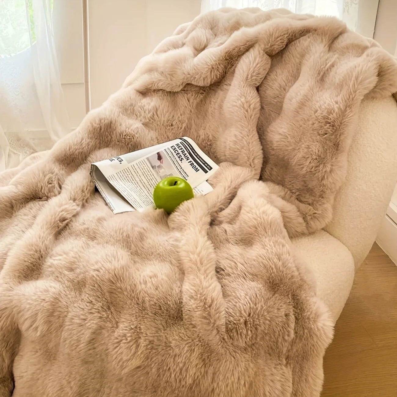 Beige fluffy blanket draped over a surface with a green apple and newspaper underneath.